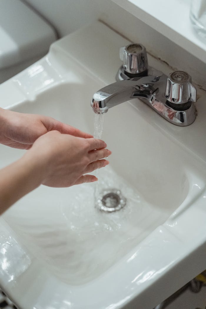 why-choose-us-02 Close-up of hands being washed under a modern stainless steel faucet in a white washbasin.